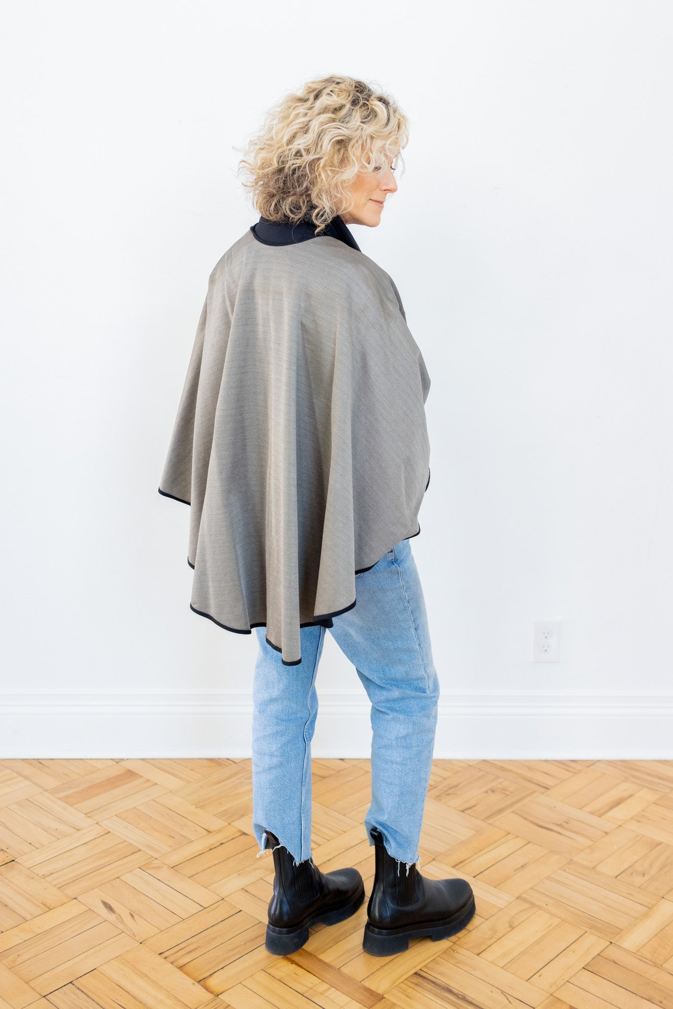 Woman wearing TRU47 Black Silver Cotton Double Knit Cape over light blue jeans and black boots, back view.