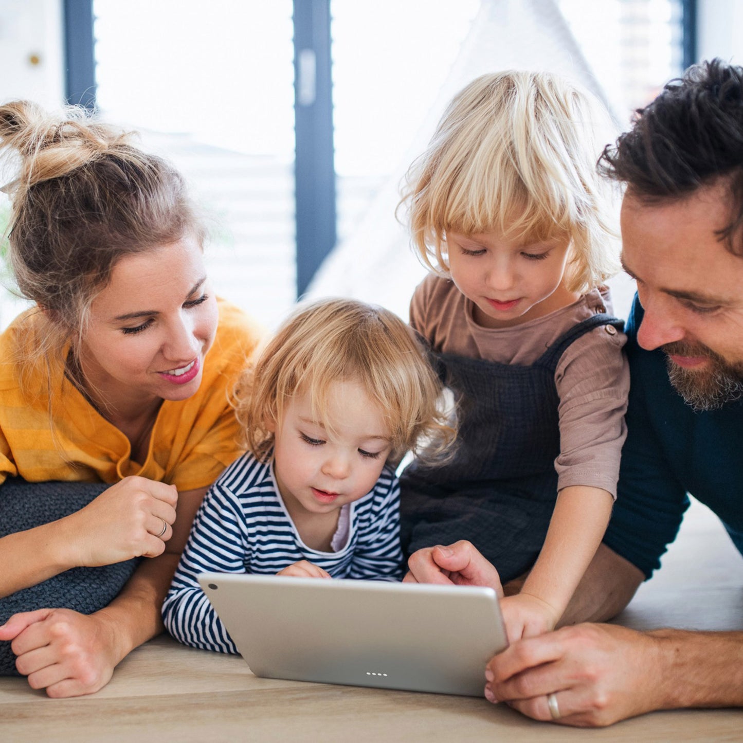 Family of four using a tablet together at a wooden table indoors.
