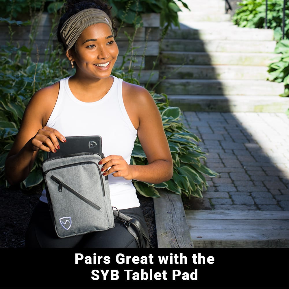 Woman holding a gray SYB Sling Bag with tablet inside, smiling at camera in outdoor garden setting.