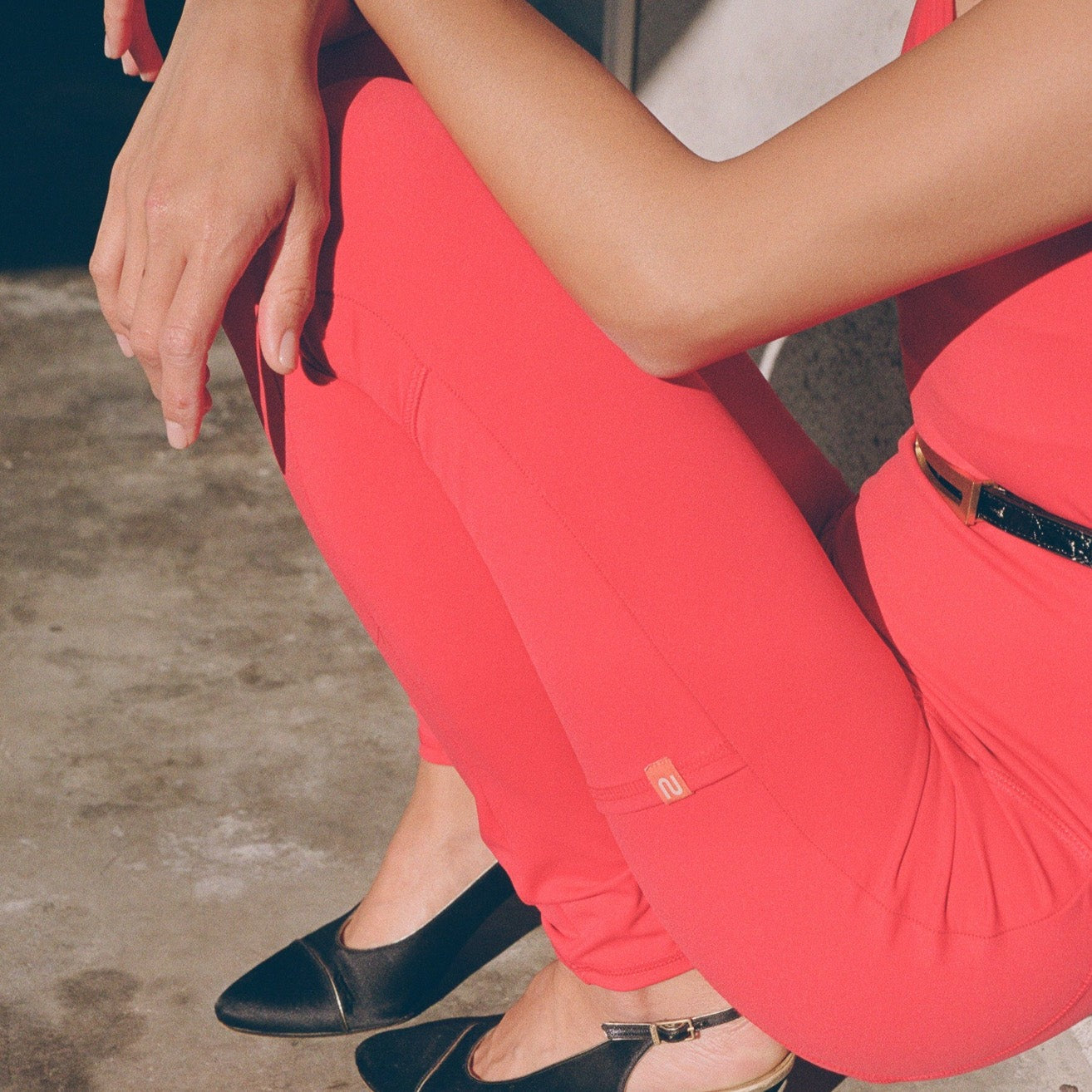 Two people wearing bright coral Even Flow Unitards with black loafers, showing the fit from waist down.