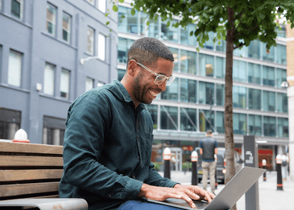 Man wearing Ocushield Amber blue light glasses while working on laptop outdoors on urban bench.
