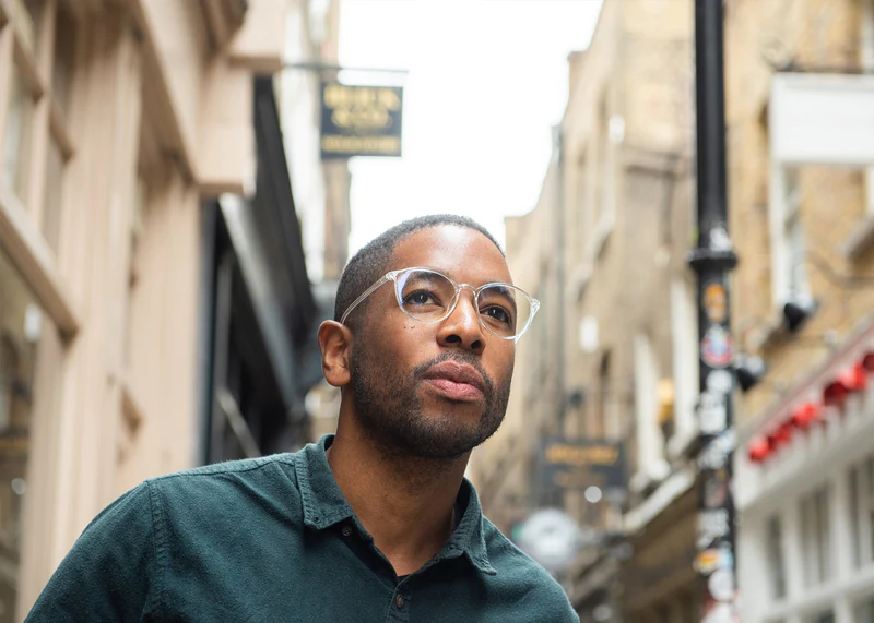Man wearing clear Ocushield All-Day Blue Light Glasses on urban street, looking upward thoughtfully.