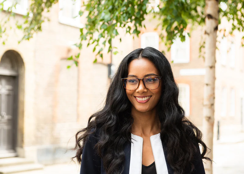 Woman wearing Ocushield Clear All-Day Blue Light Glasses outdoors, smiling at camera against historic building backdrop.