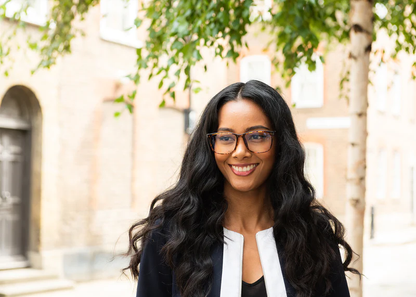 Woman wearing Ocushield Clear All-Day Blue Light Glasses outdoors, smiling at camera against historic building backdrop.