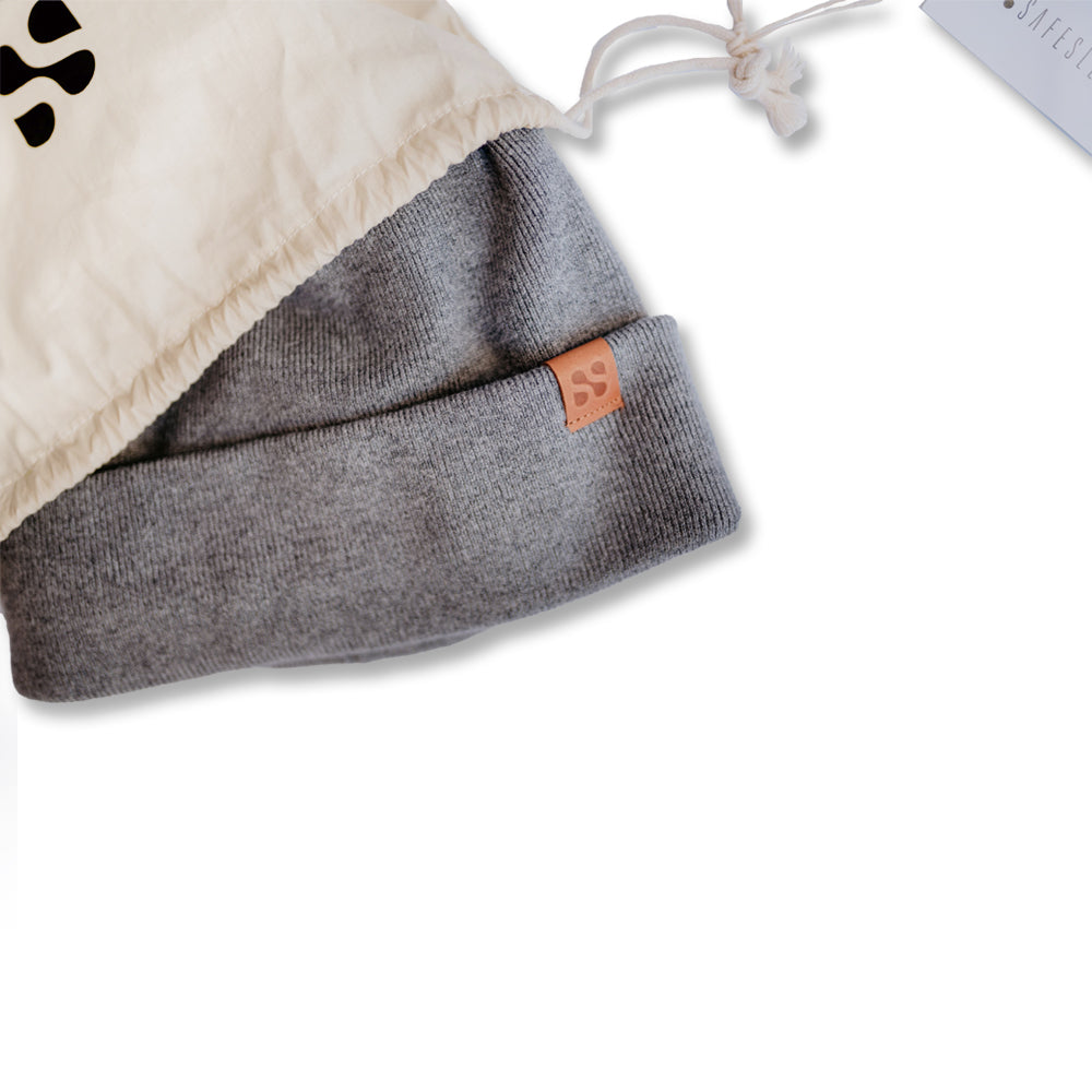 SafeSleeve Beanie in gray folded in cream drawstring bag with leather brand label visible.