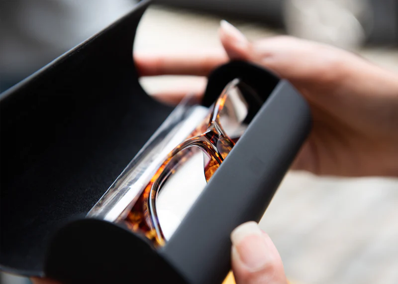 Ocushield Clear blue light glasses with tortoiseshell frames displayed in black packaging, held open to show the eyewear inside.