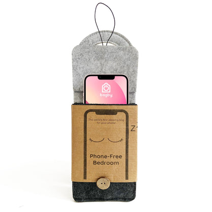 Bagby phone sleeping bag displayed with a smartphone inside the gray felt pouch, showing the kraft paper band labeled "Phone-Free Bedroom" with hanging loop.
