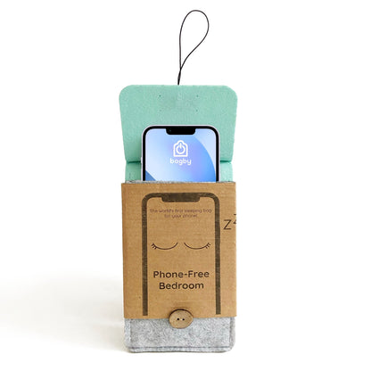 Bagby phone sleeping bag displayed with smartphone inside, showing turquoise felt exterior and kraft cardboard packaging labeled "Phone-Free Bedroom."