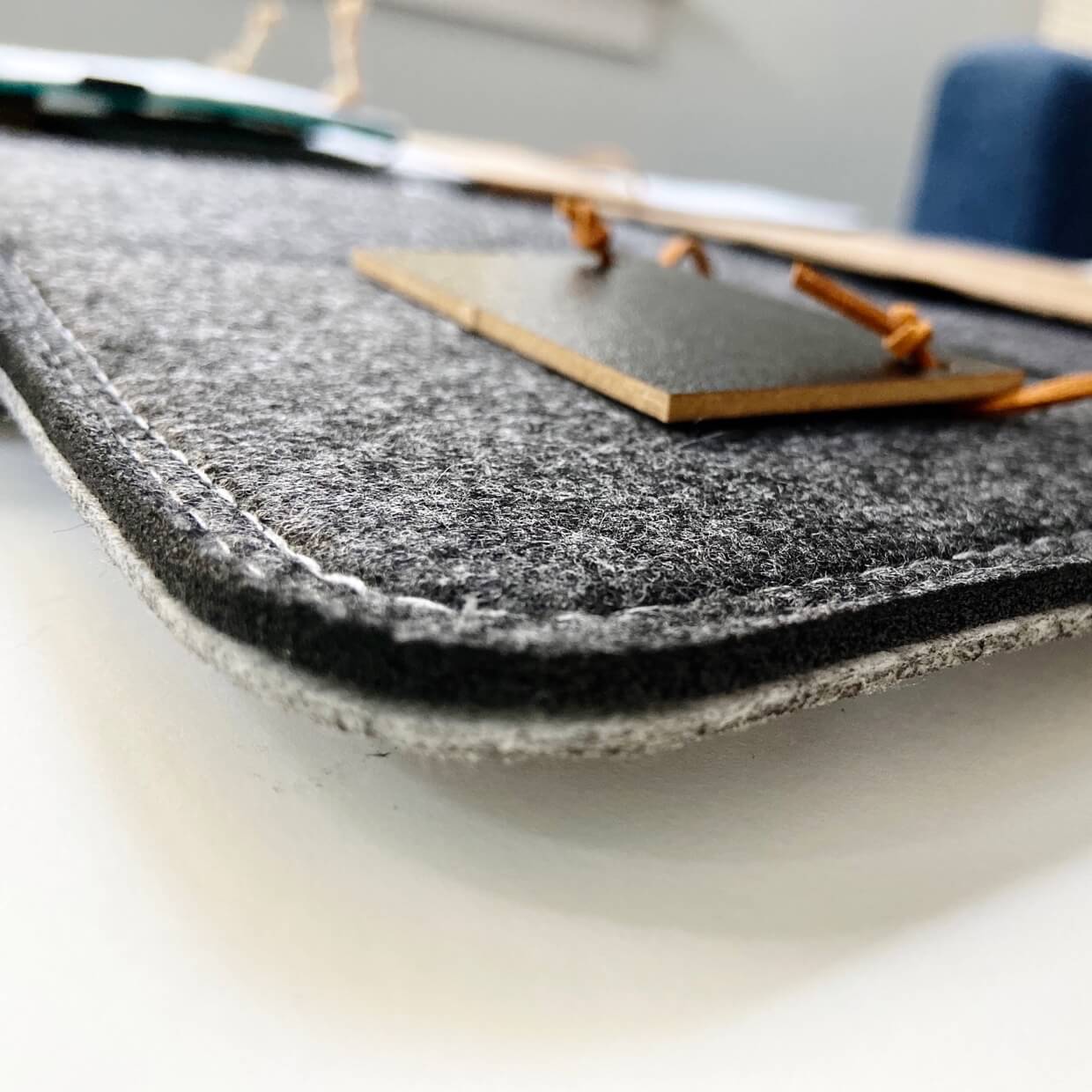 Close-up of Bagby 4 Pocket Phone Holder showing textured gray fabric surface with stitched edge detail and wooden accessories nearby.