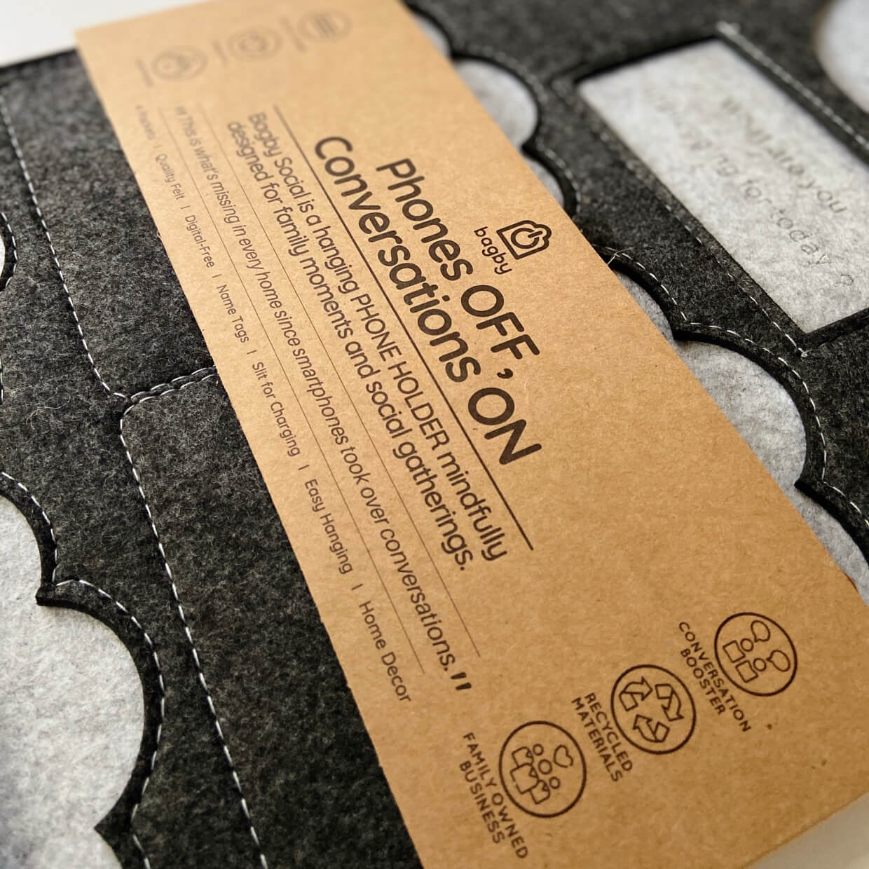 Bagby 4 Pocket Phone Holder instruction tag showing care symbols and product details on charcoal fabric with white stitching.