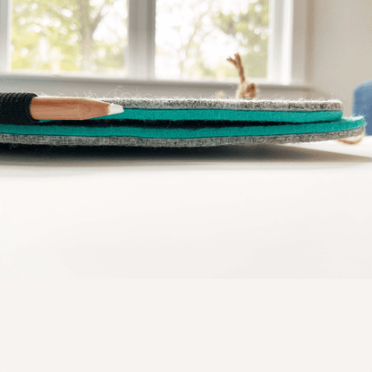 Bagby 4 Pocket Phone Holder displayed flat, showing layered gray and teal felt construction with a paintbrush resting on top near a bright window.