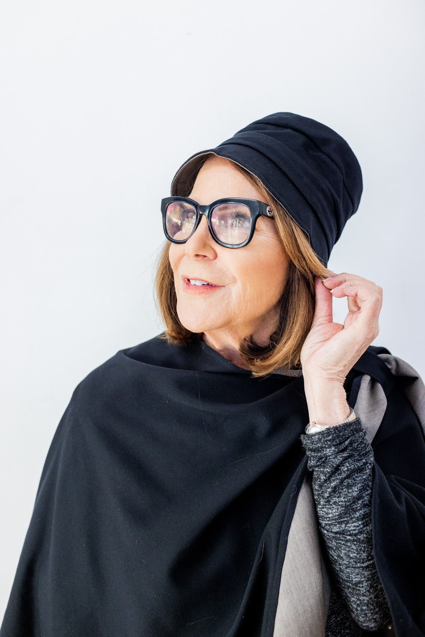 Woman wearing black TRU47 bucket hat with glasses, adjusting hat brim while looking to the side against white background.