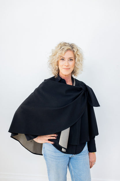 Woman wearing black TRU47 cotton double knit cape over gray top and blue jeans, front view against white background.