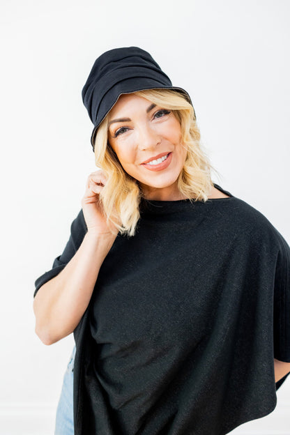 Woman wearing black TRU47 bucket hat with blonde wavy hair, smiling at camera against white background