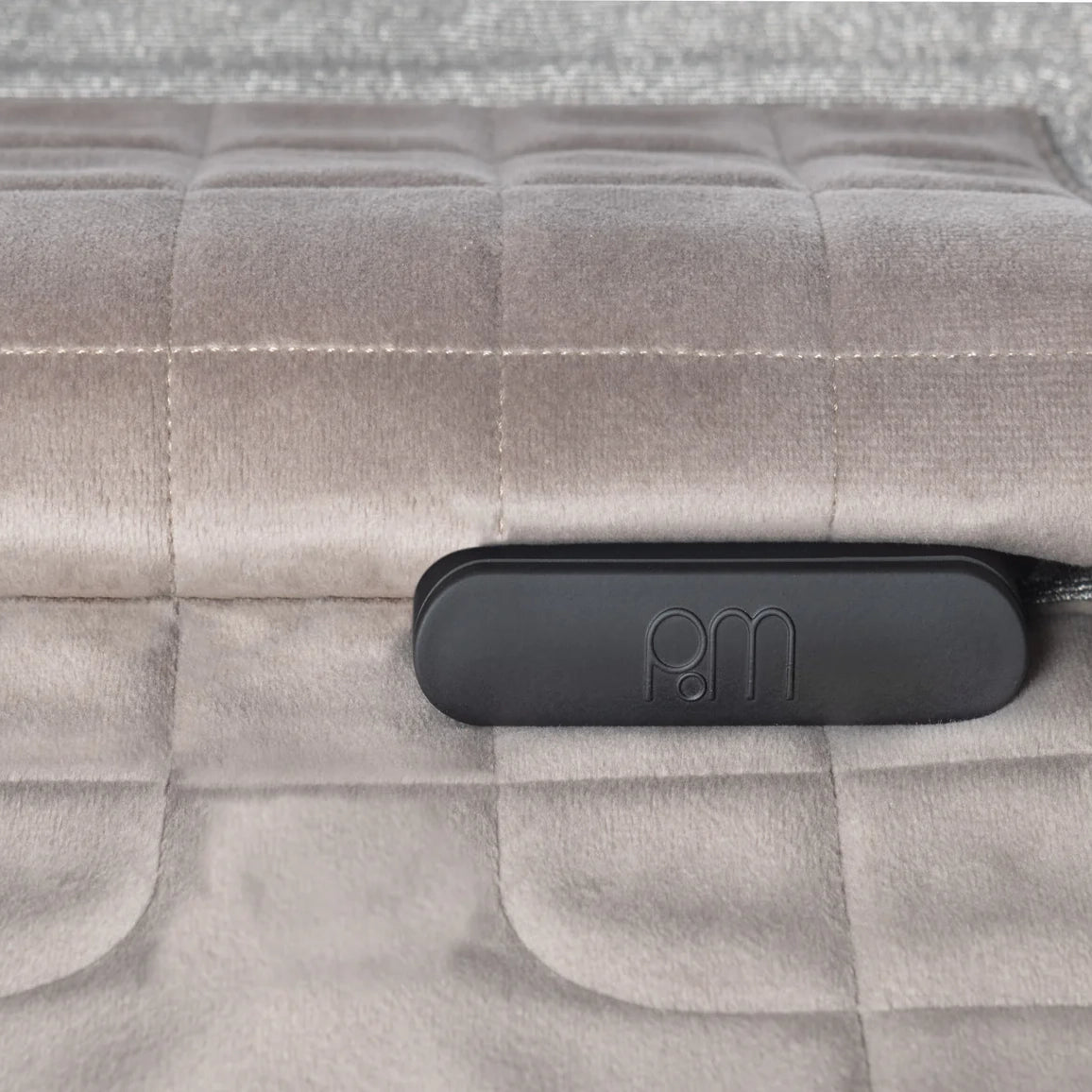 PoM Shield ORIGINAL phone Faraday cage with black handle detail resting on quilted beige fabric surface.