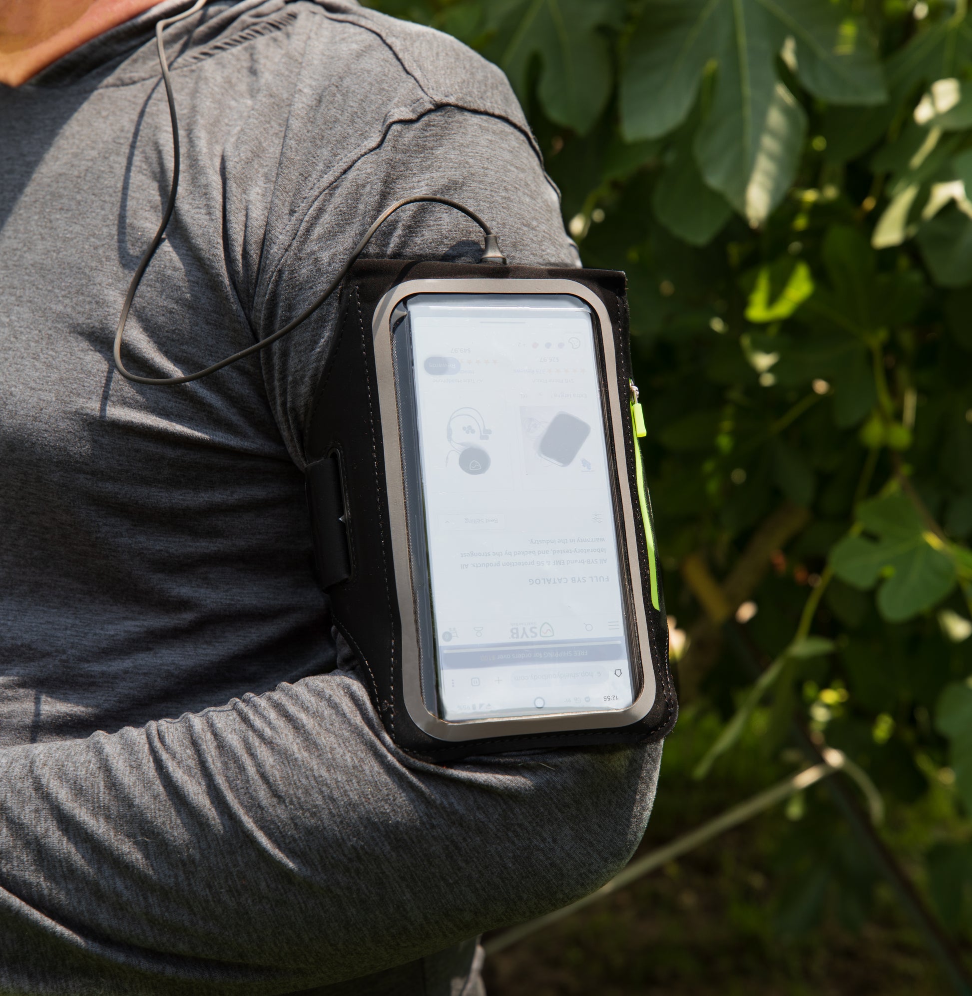 Person wearing SYB Arm Band Phone Pouch on bicep with smartphone inside, outdoors with green foliage background.