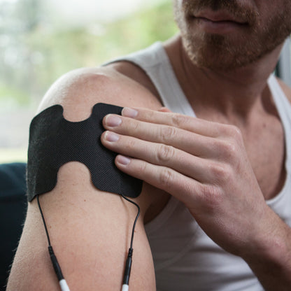 Man applying black TENS electrode pad to shoulder during iReliev TENS therapy session.