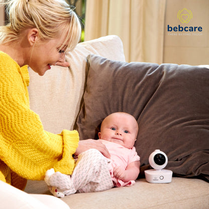 Mother in yellow sweater holding infant on couch with Bebcare WiFi baby monitor positioned nearby.