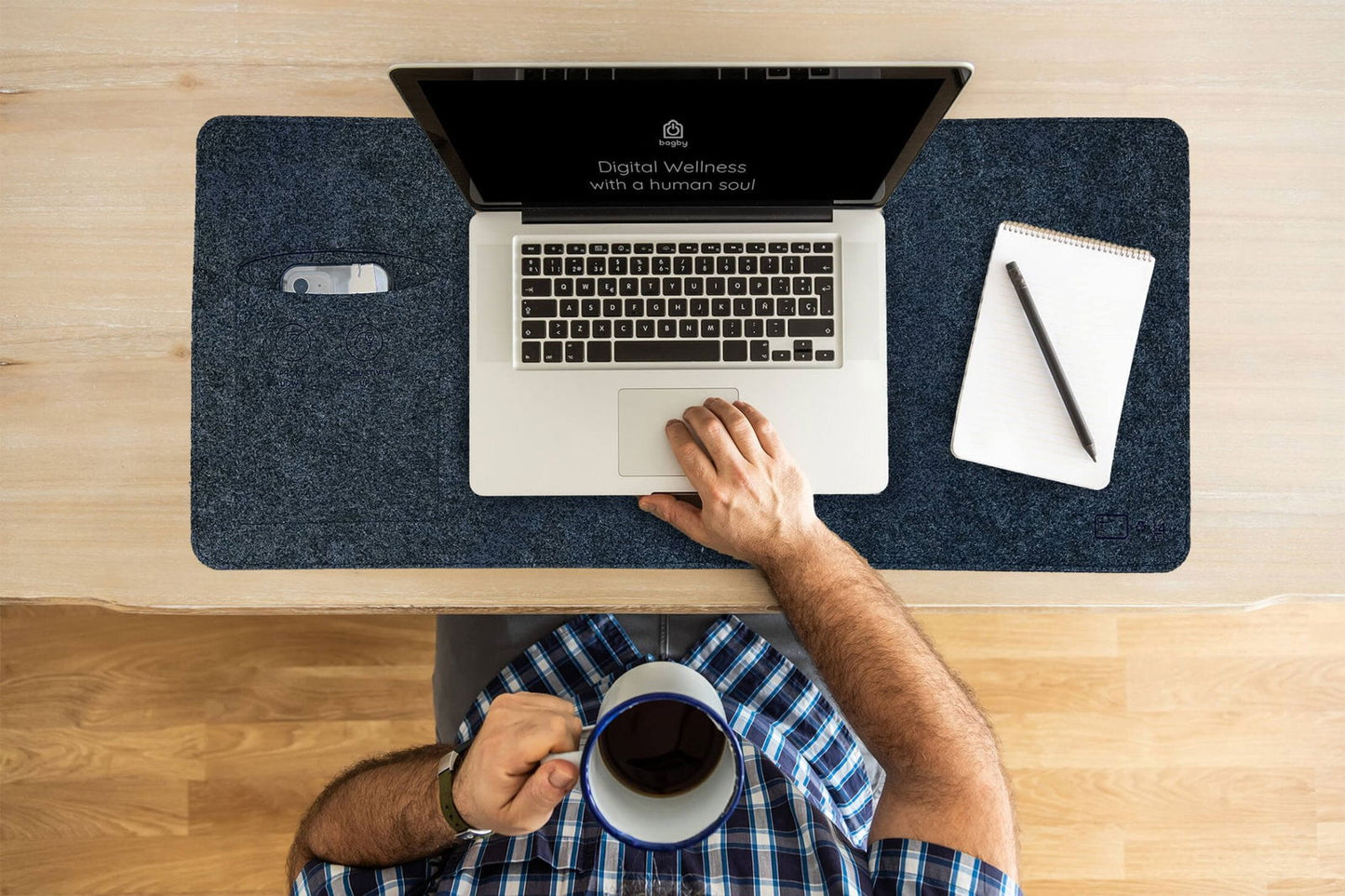 Overhead view of a person typing on a laptop resting on a navy Bagby MAT, with a coffee mug, notepad and a phone in the side pocket.