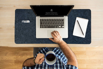 Overhead view of a person typing on a laptop resting on a navy Bagby MAT, with a coffee mug, notepad and a phone in the side pocket.