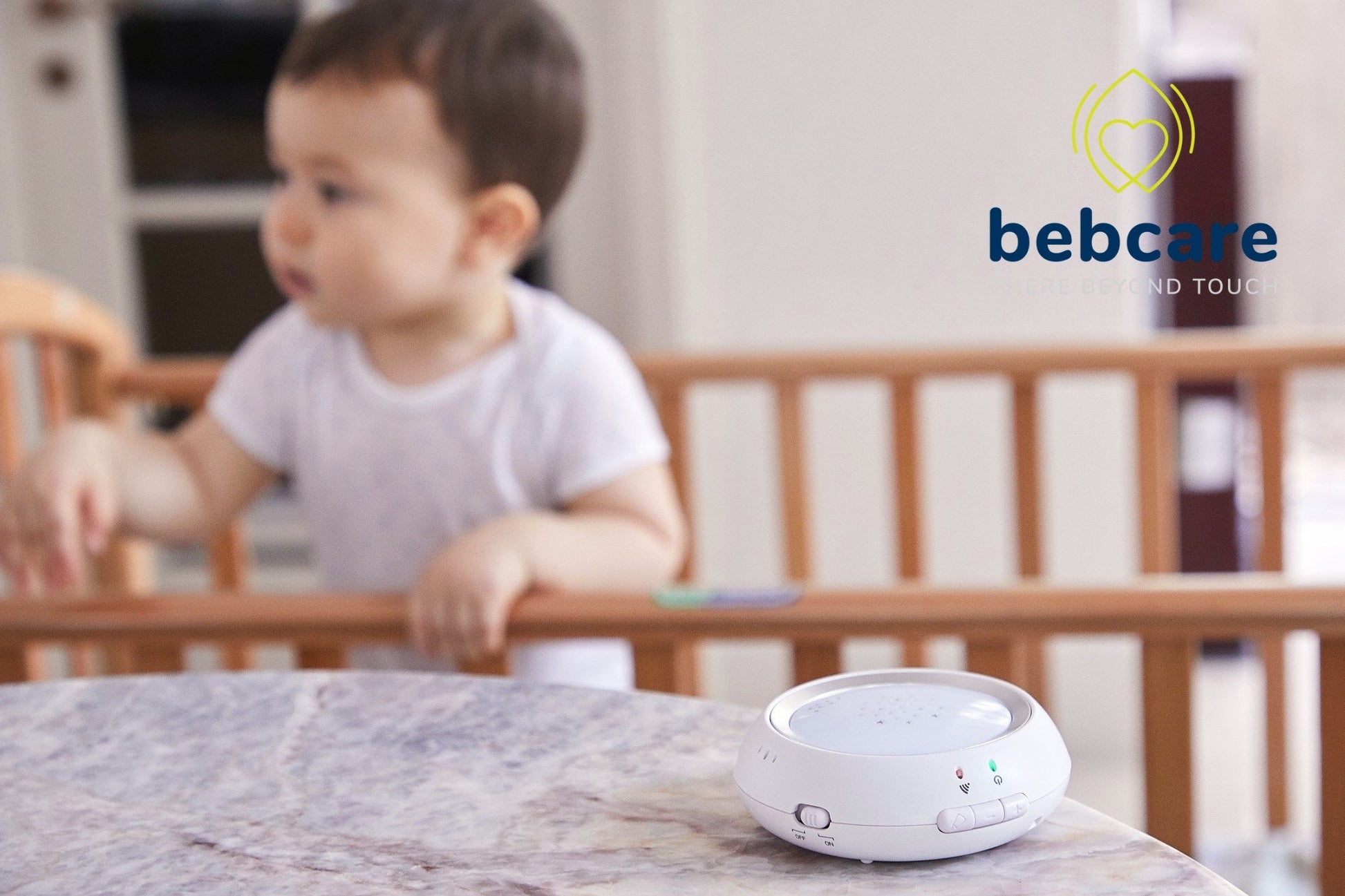 Bebcare baby monitor displayed on surface with toddler in crib background, showing device screen and control buttons.