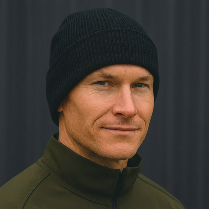 Man wearing black ribbed HAVN WaveStopper™ Beanie and olive green jacket against dark background, front view.