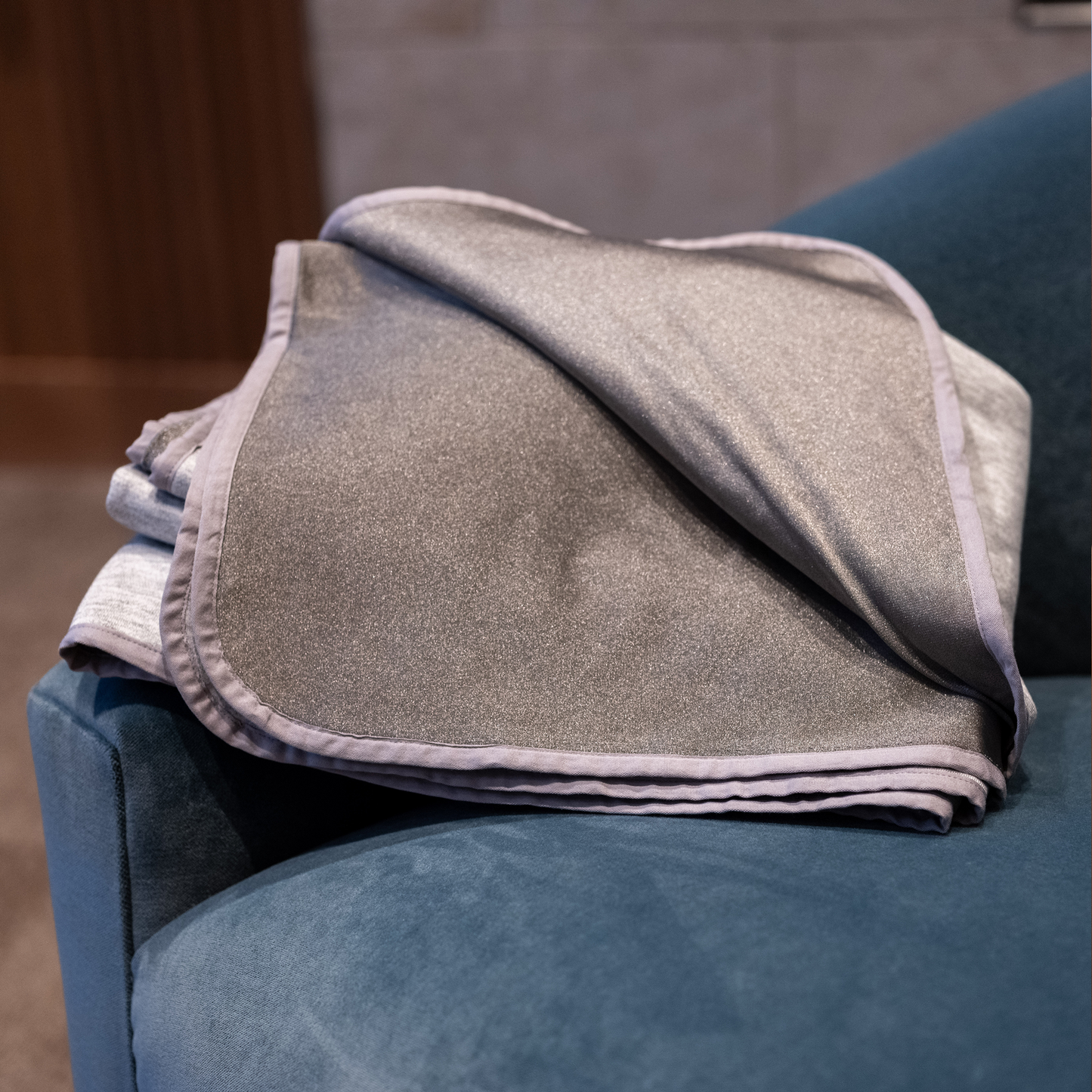 HAVN WaveStopper™ Blanket draped over a blue armchair, showing the gray fabric and finished edges in a home setting.