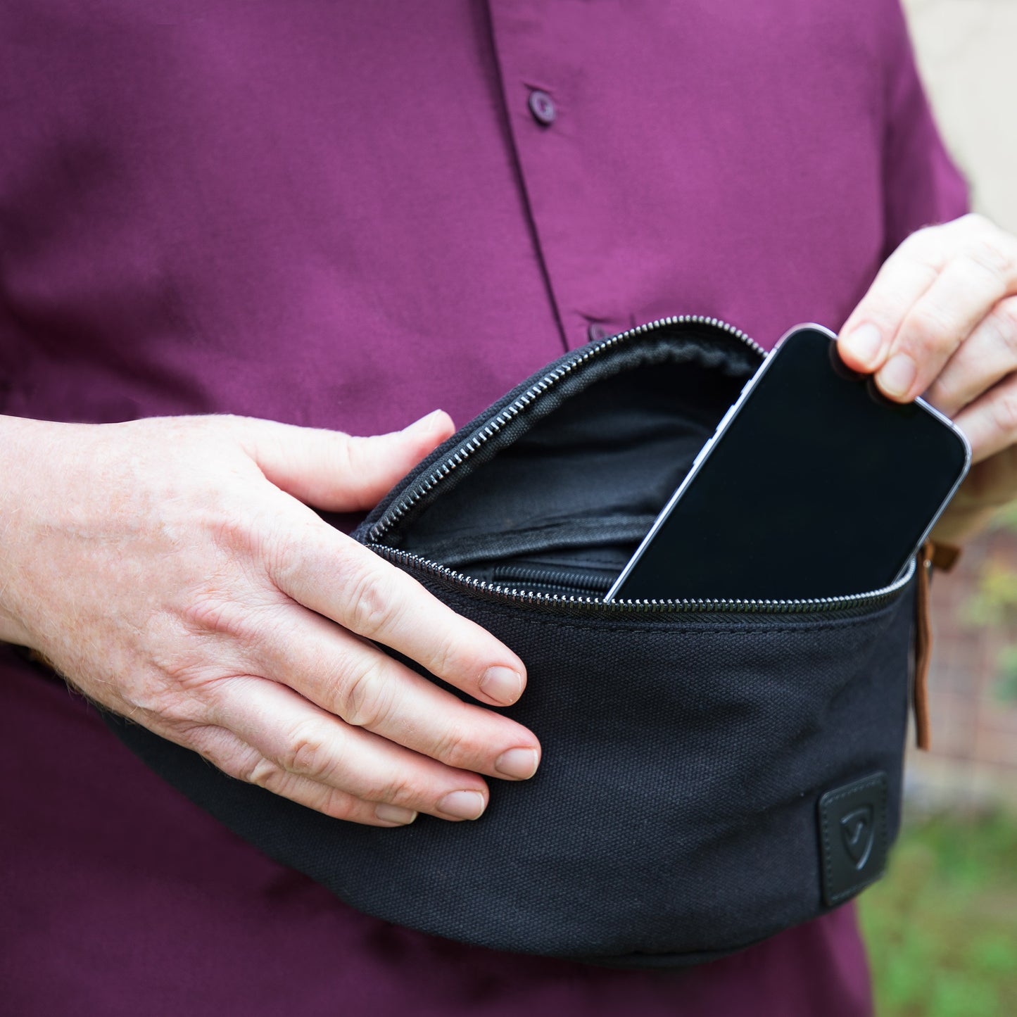 Person in purple shirt opening black SYB Cross Body Fanny Pack, showing zippered interior compartment.
