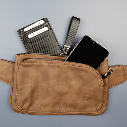 SYB Cross Body Fanny Pack in tan vegan leather displayed open, showing interior contents including a carbon fiber wallet, black comb, and smartphone.