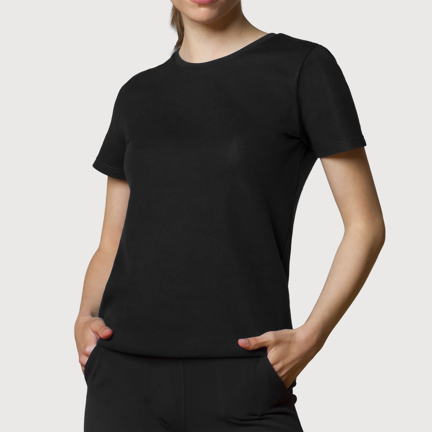 Woman wearing black HAVN WaveStopper™ T-Shirt 2.0 with hands in pockets, front view against white background.