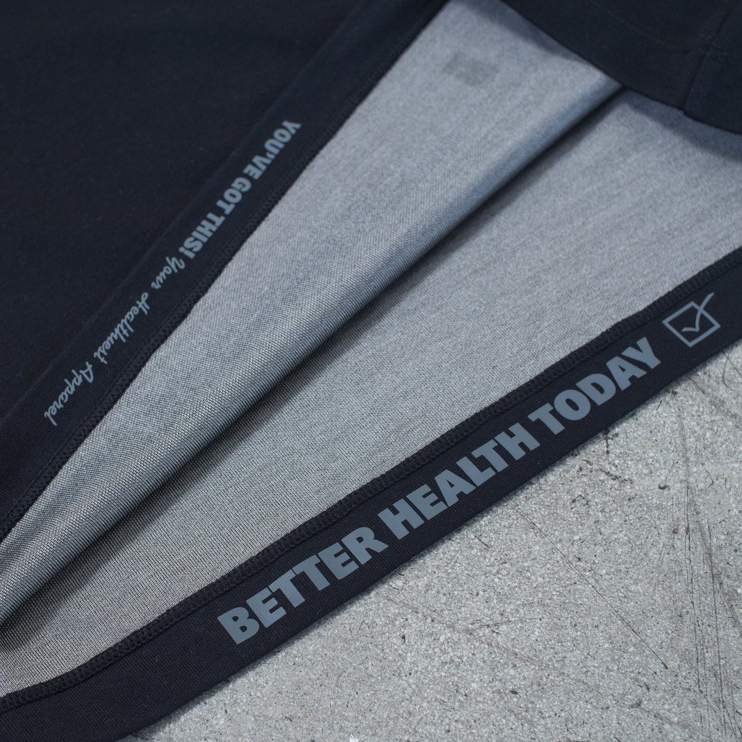 Folded HAVN WaveStopper™ T-Shirt 2.0 displaying black waistband with "BETTER HEALTH TODAY" text and gray fabric layers on concrete surface.