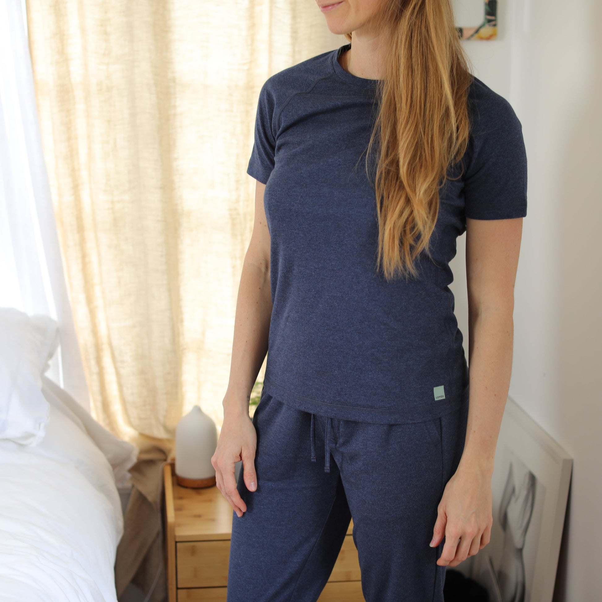 Woman wearing navy HAVN WaveStopper™ Pajama Set with short-sleeve shirt and matching pants, standing indoors near window with cream curtains.