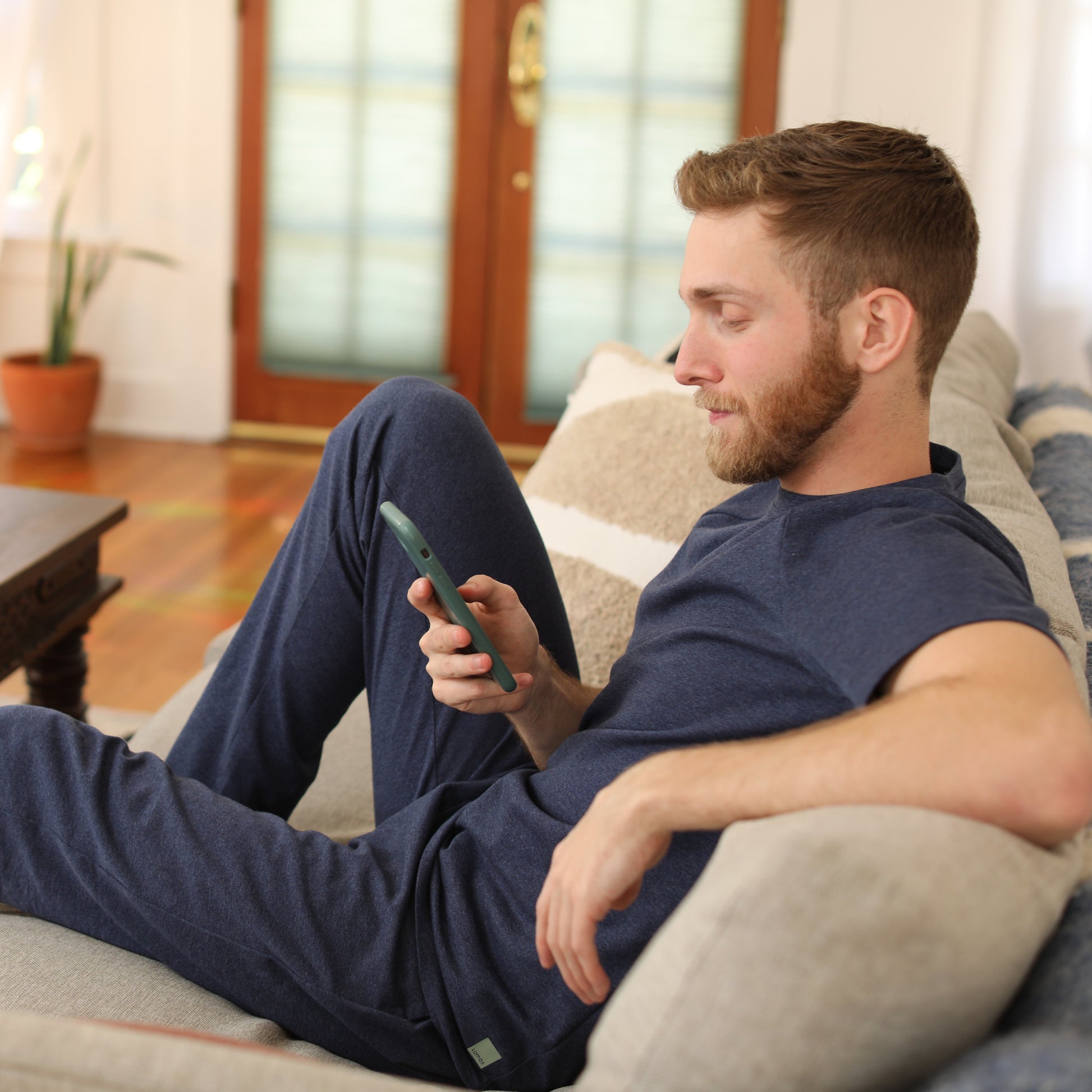 Man wearing navy HAVN WaveStopper™ Pajama Set relaxing on couch with phone, lifestyle in-use shot.