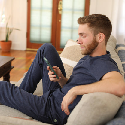 Man wearing navy HAVN WaveStopper™ Pajama Set relaxing on couch with phone, lifestyle in-use shot.