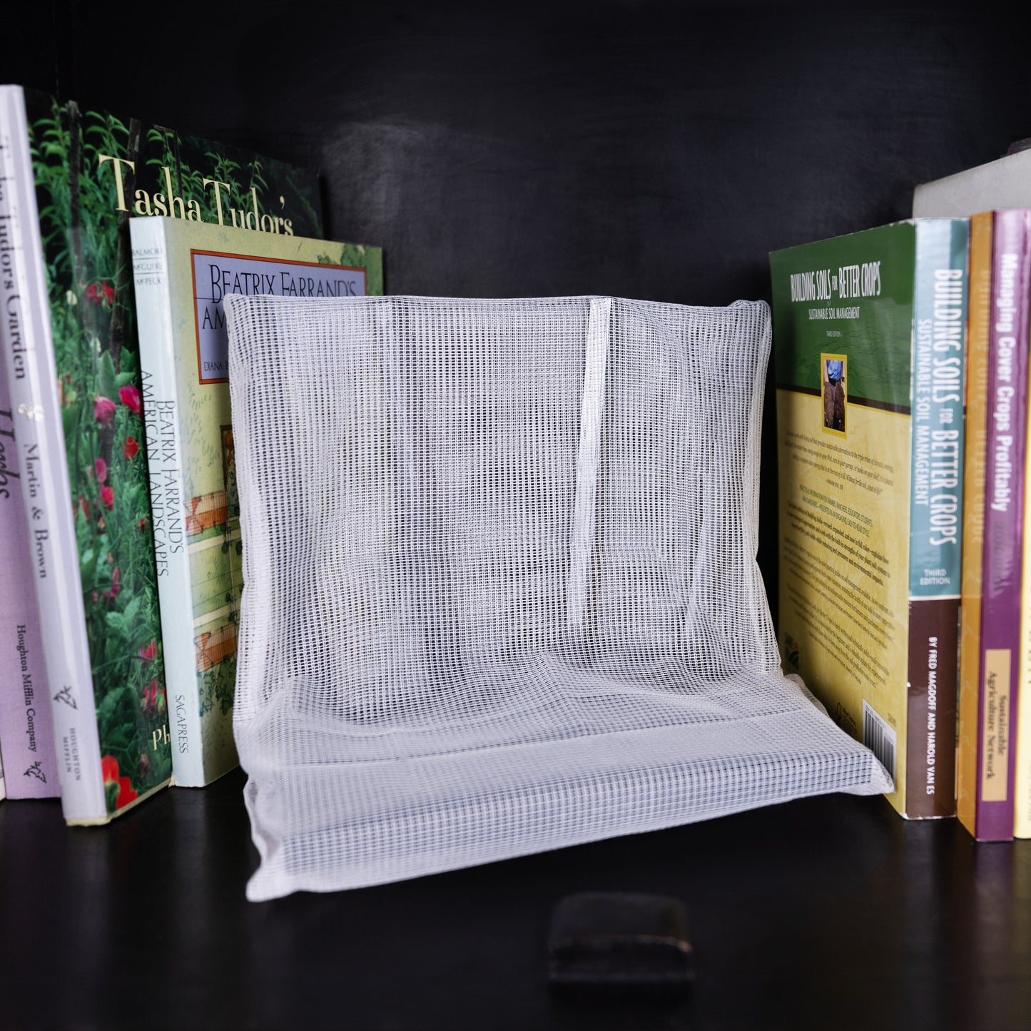WiFi Signal Tamer white mesh pouch displayed between stacked books on dark shelf.