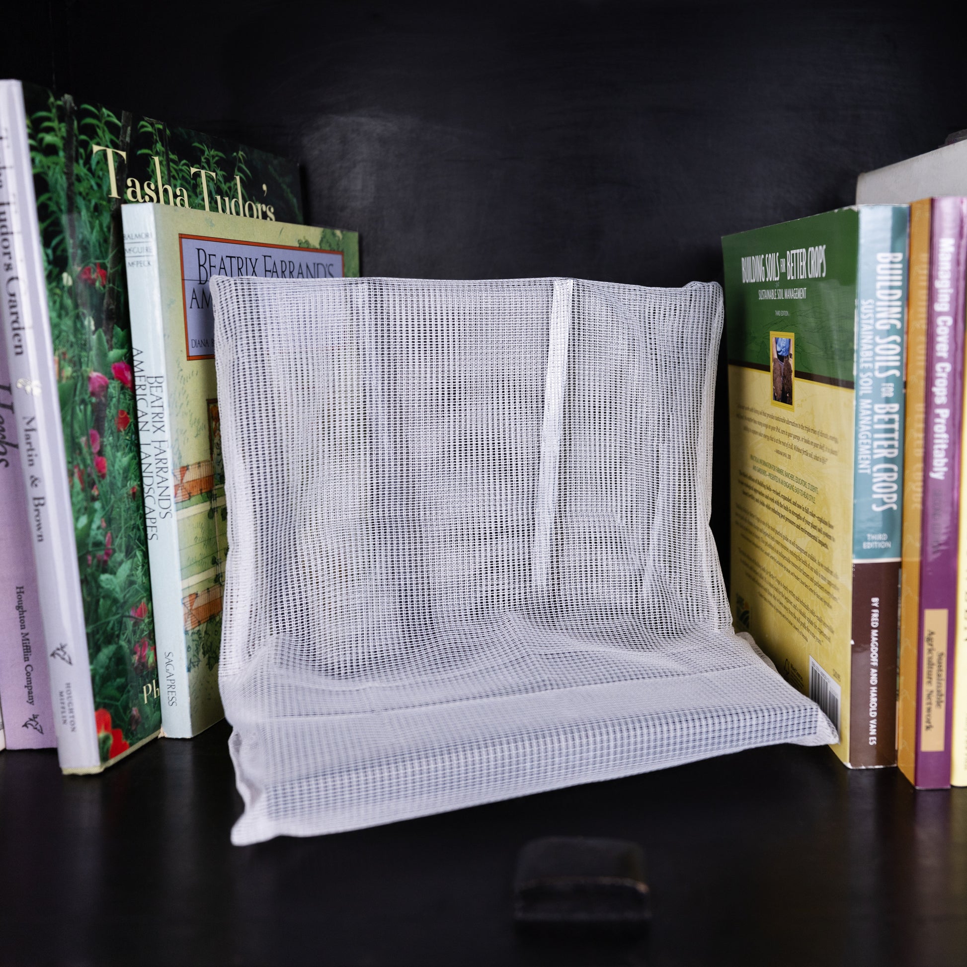 WiFi Signal Tamer white mesh pouch displayed between stacked books on dark shelf.