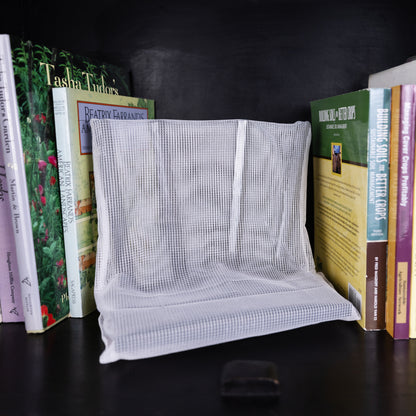 WiFi Signal Tamer white mesh pouch displayed between stacked books on dark shelf.