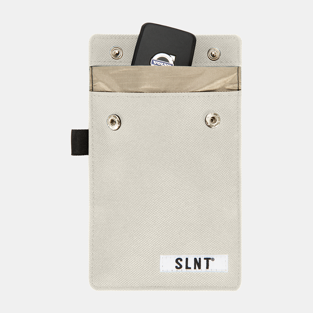 Faraday Key Fob Bag in cream canvas with open flap revealing black key fob inside and tan interior pocket, SLNT branding visible.