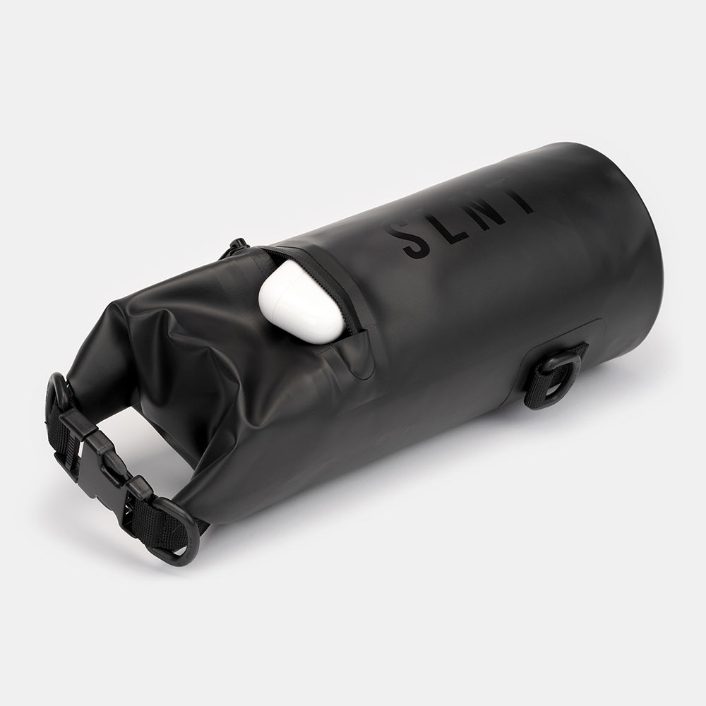 SLNT Faraday Dry Bag with white earbuds inside, rolled closed with black straps and attachment points visible.