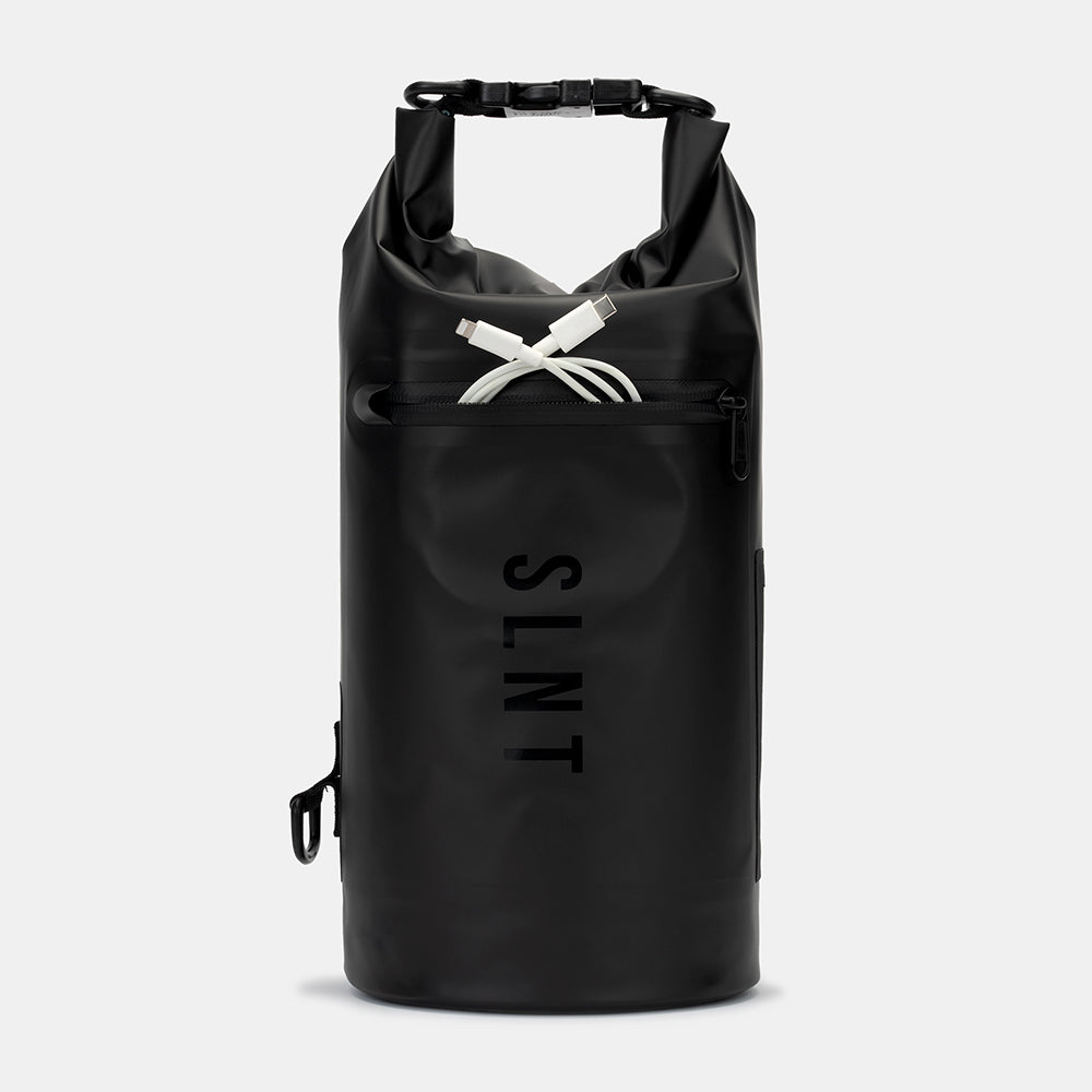 SLNT Faraday Dry Bag in black with rolled top handles, displaying a white charging cable stored in the front pocket.