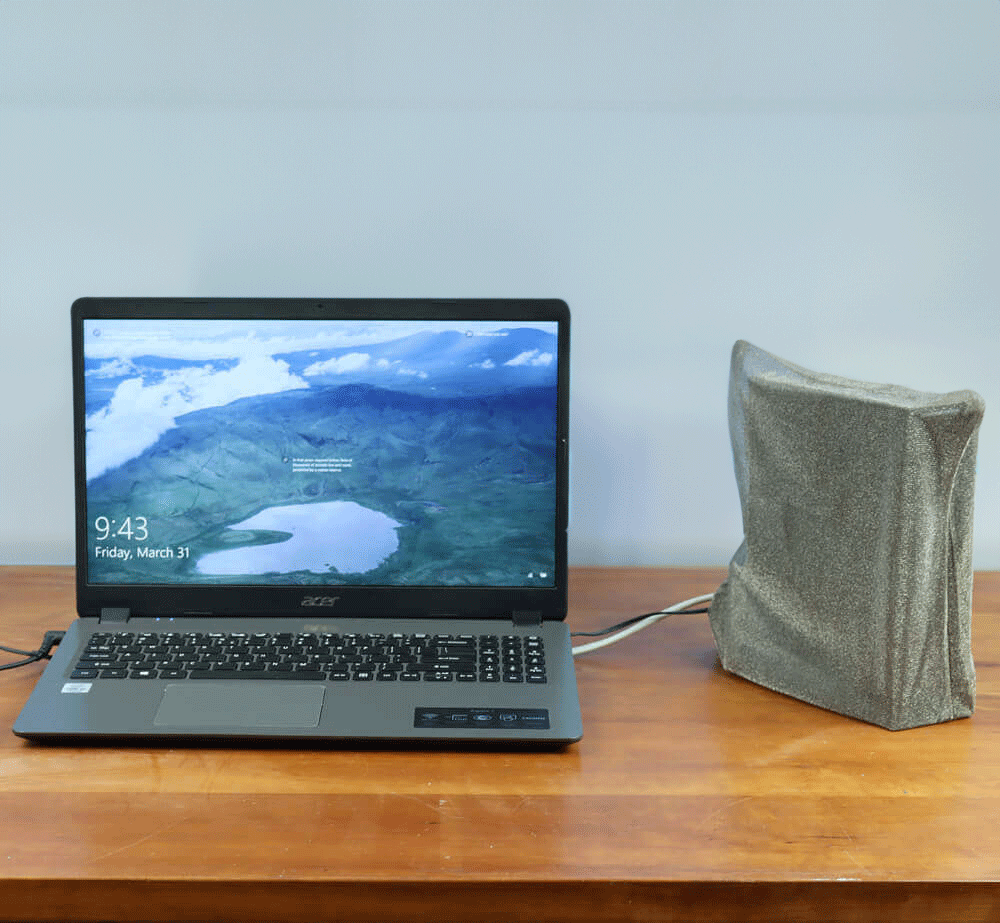 Acer laptop displaying aerial landscape on screen next to gray fabric WiFi Signal Tamer pouch on wooden desk.
