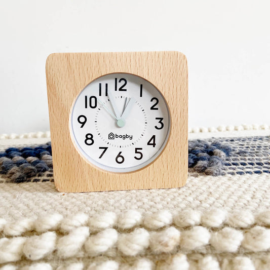 Beech wood Bagby FARMHOUSE alarm clock reading just before one o'clock, set on a woven blue and cream textile surface.