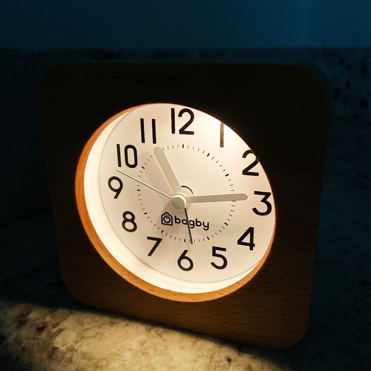 Beech wood Bagby FARMHOUSE alarm clock lit by its built-in night light in a dark room, dial reading about 10:15.