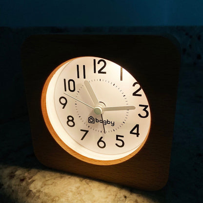 Beech wood Bagby FARMHOUSE alarm clock lit by its built-in night light in a dark room, dial reading about 10:15.