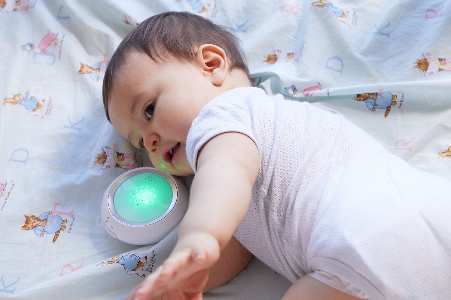 Baby using Bebcare Low-EMF Digital Audio Baby Monitor with glowing green light on patterned bedding.