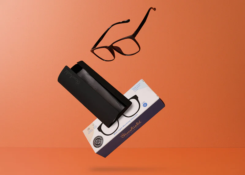 Ocushield Clear All-Day Blue Light Glasses displayed with black carrying case and packaging on orange background.