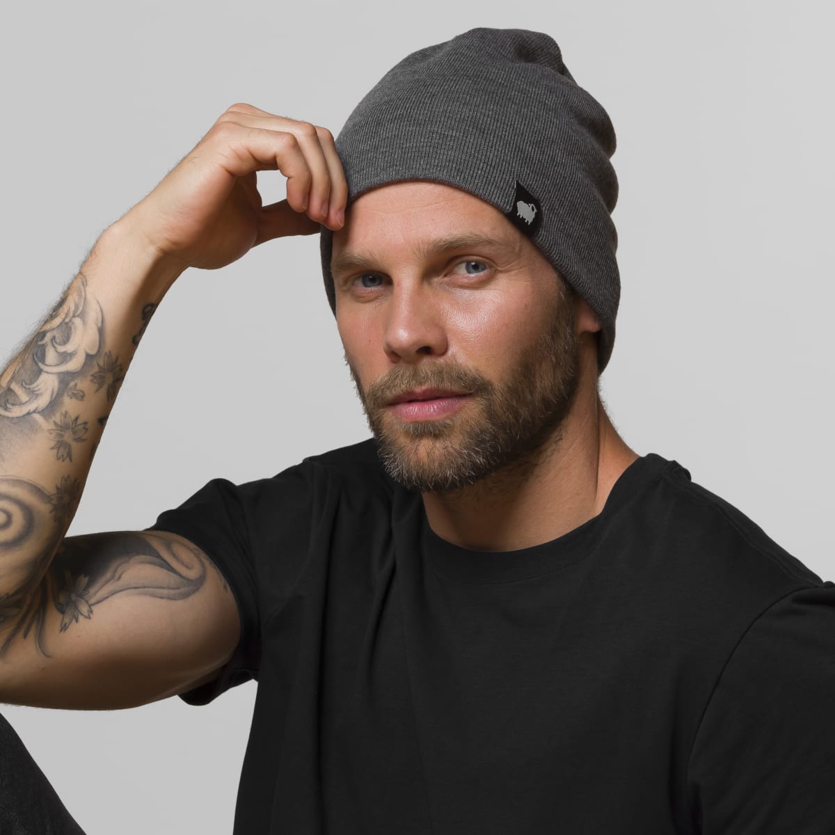 Man wearing charcoal gray HAVN WaveStopper™ Beanie with black t-shirt, adjusting hat with hand, front view.