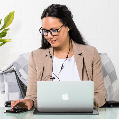 Woman wearing glasses and headset working at laptop on SYB Laptop Pad, seated at desk with plant nearby.