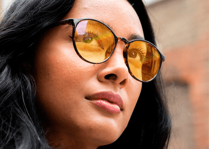 Woman wearing Ocushield Amber dark blue light glasses with tortoiseshell frames, side profile view against blurred brick background.