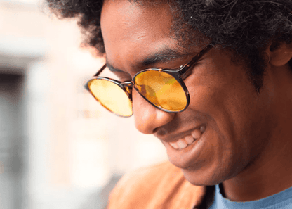 Man wearing Ocushield Amber blue light glasses with yellow-tinted lenses, smiling outdoors in natural sunlight.